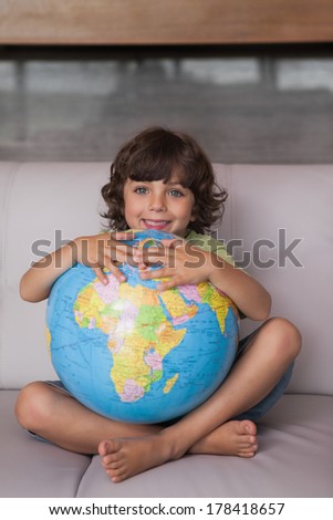 Portrait of a happy young kid with globe sitting in the living room at home