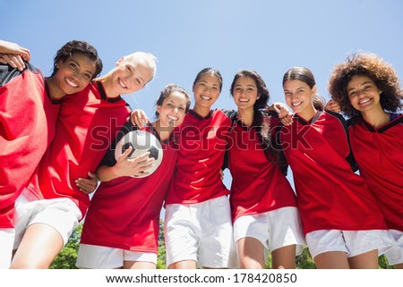 Portrait of confident female soccer team with ball against clear blue sky