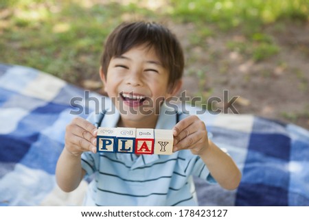High angle portrait of a happy young boy holding block alphabets as \'play\' at the park