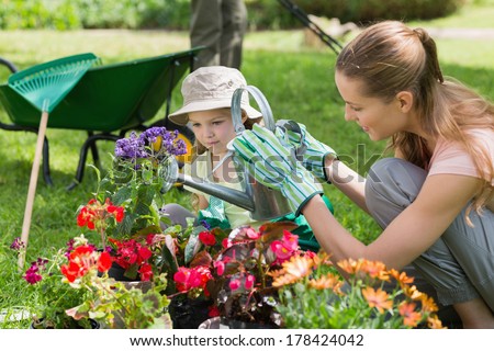 Side view of a mother and daughter watering plants at the garden