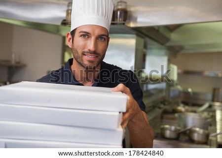 Happy pizza chef holding stack of pizza boxes in a commercial kitchen