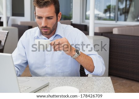 Concentrating businessman working with laptop drinking coffee in patio of restaurant