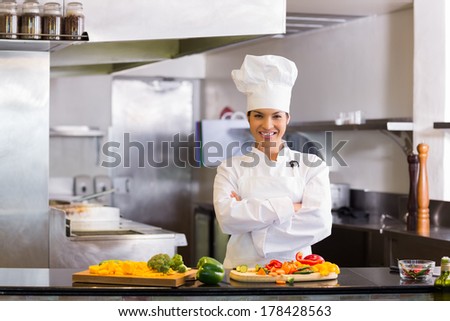 Portrait of a smiling young female chef standing with cut vegetables in the kitchen