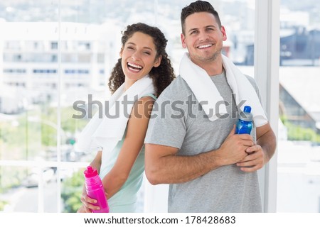 Portrait of cheerful couple with towels and water bottles at gym