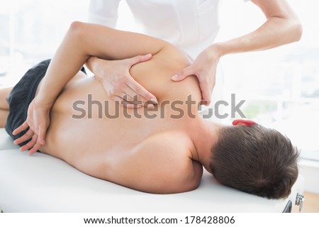 Professional female physiotherapist giving shoulder massage to man in hospital