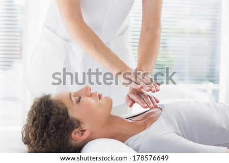 Female therapist performing Reiki over woman at health spa