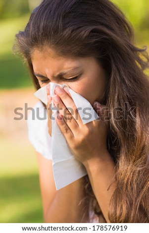 Close-up of a young woman blowing nose with tissue paper at the park