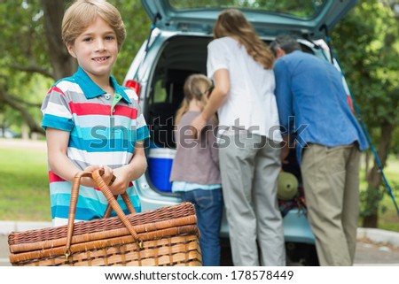 Portrait of a boy with picnic basket while family in background at car trunk
