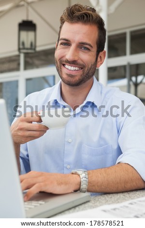 Happy young businessman working at laptop drinking coffee in patio of restaurant