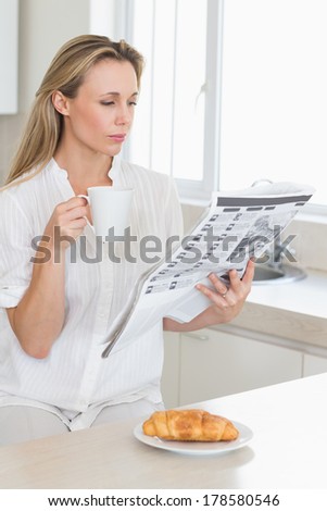 Serious woman holding mug and newspaper at breakfast at home in the kitchen