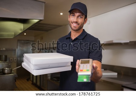 Cheerful pizza delivery man holding credit card machine in a commercial kitchen