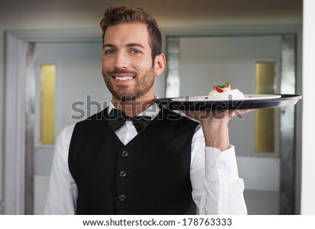 Smiling waiter holding tray with plate of dessert in a fancy restaurant