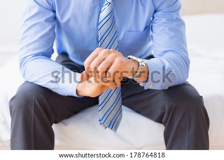 Businessman sitting on bed checking the time at home in bedroom