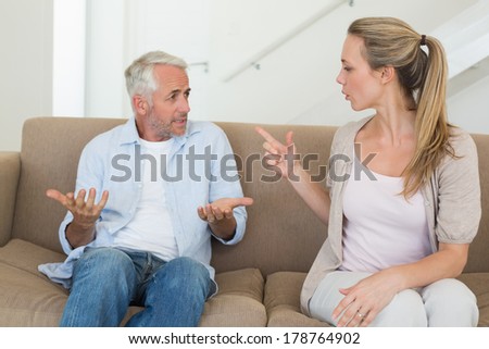 Angry couple sitting on couch arguing at home in the living room