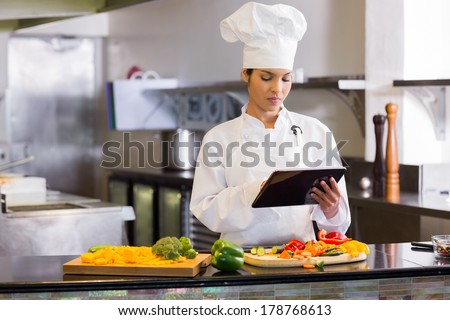Concentrated young female chef using digital tablet while cutting vegetables in the kitchen
