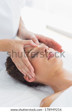 Relaxed young woman receiving massage on forehead in health spa