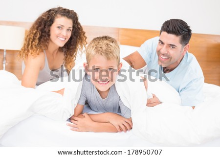 Cute young family smiling at camera on bed at home in bedroom