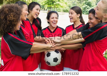 Excited female soccer team stacking hands on ball at park