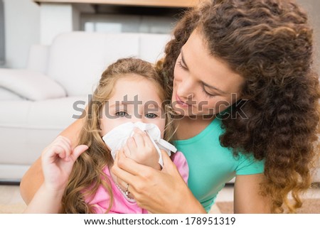 Mother helping her daughter blow her nose at home in living room
