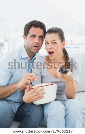 Couple watching scary movie on the sofa with bowl of popcorn at home in the living room