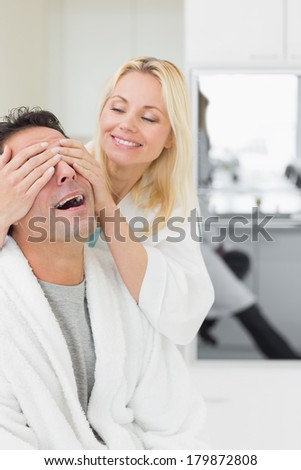 Smiling woman covering happy mans eyes in the kitchen at home
