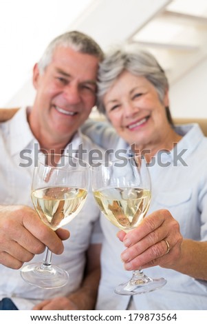 Senior couple sitting on couch having white wine at home in living room