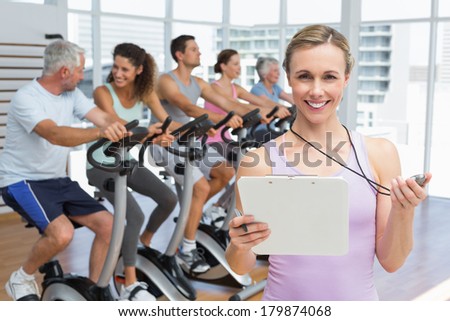 Portrait of a female trainer with people working out at exercise bike class in gym