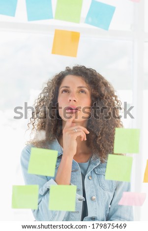 Thinking pretty designer looking at sticky notes on window in creative office