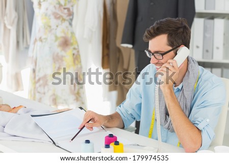 Side view of a smiling young male fashion designer using phone in the studio