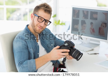 Handsome photographer holding his camera smiling at camera in creative office