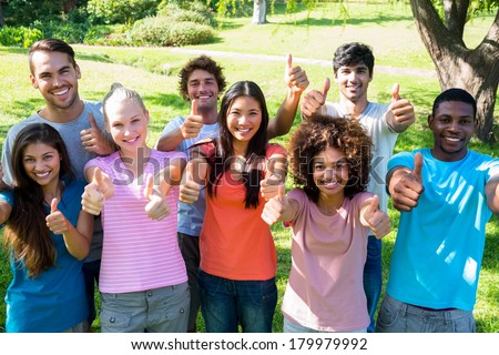 Group portrait of happy friends gesturing thumbs up at college campus