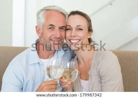Happy couple sitting on couch toasting with white wine at home in the living room