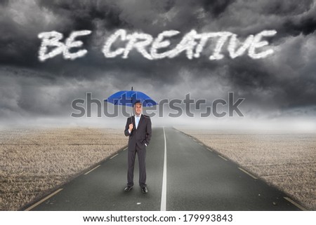 The word be creative and businessman smiling at camera and holding blue umbrella against misty brown landscape with street
