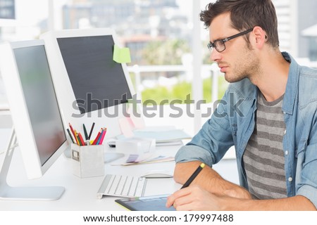 Side view of a casual male photo editor using graphics tablet in a bright office
