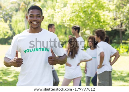Portrait of smiling volunteer showing thumbs up with friends disucssing in background
