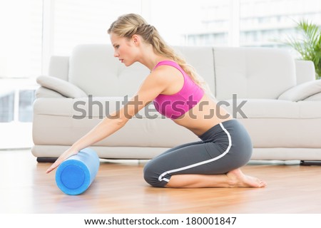 Fit blonde kneeling on floor using foam roller at home in the living room