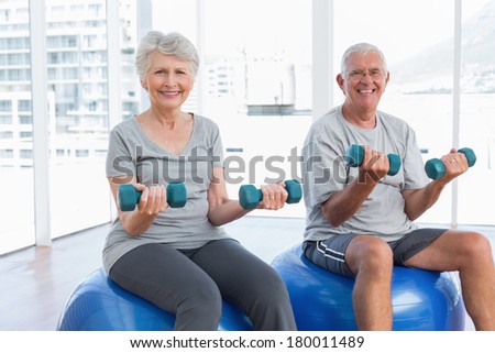 Happy senior couple sitting on fitness balls with dumbbells in the medical office