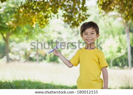 Portrait of a happy young boy playing with a paper plane at the park