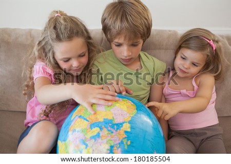 Three young kids with globe sitting in the living room at home