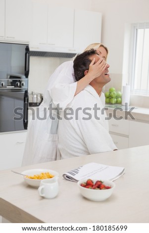 Side view of a woman covering man\'s eyes at breakfast table in the kitchen at home