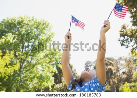 Low angle view of a young girl holding up two American flags at the park