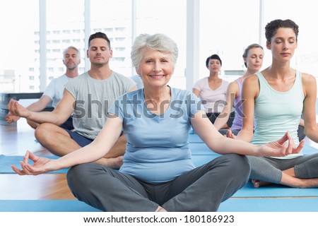 Sporty people sitting in lotus pose at a bright fitness studio