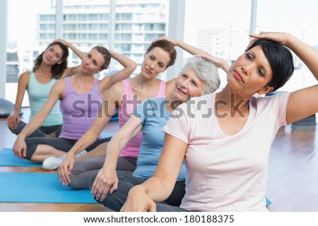 Female trainer with class stretching neck in row at yoga class