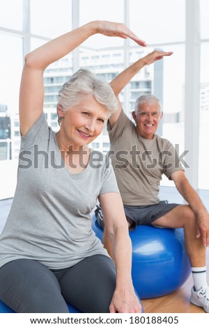 Happy senior couple doing stretching exercises on fitness balls in the medical office