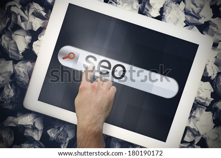 Hand touching the word seo on search bar on tablet screen on crumpled papers