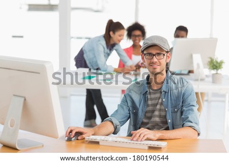 Portrait of casual male artist using computer with colleagues in the background at a bright office