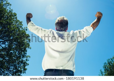 Successful businessman with arms outstretched against clear blue sky