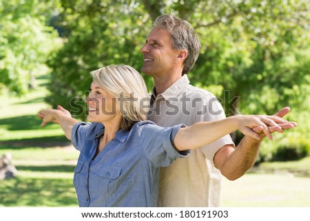 Happy couple standing with arms outstretched in park