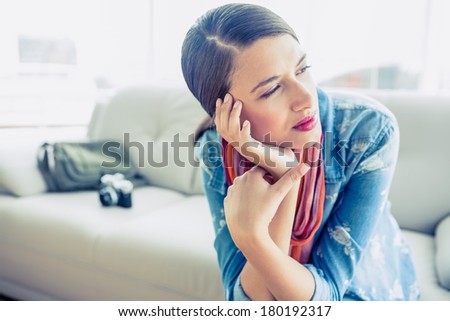 Pretty brunette sitting on sofa looking away at home in the living room