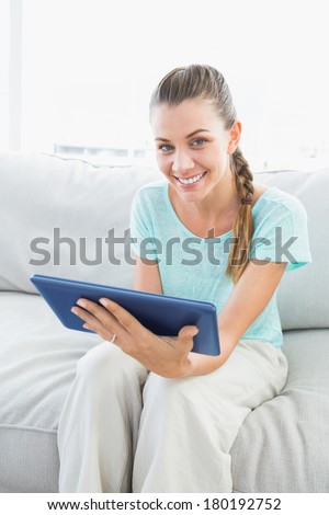 Smiling woman sitting on couch using tablet pc at home in the living room